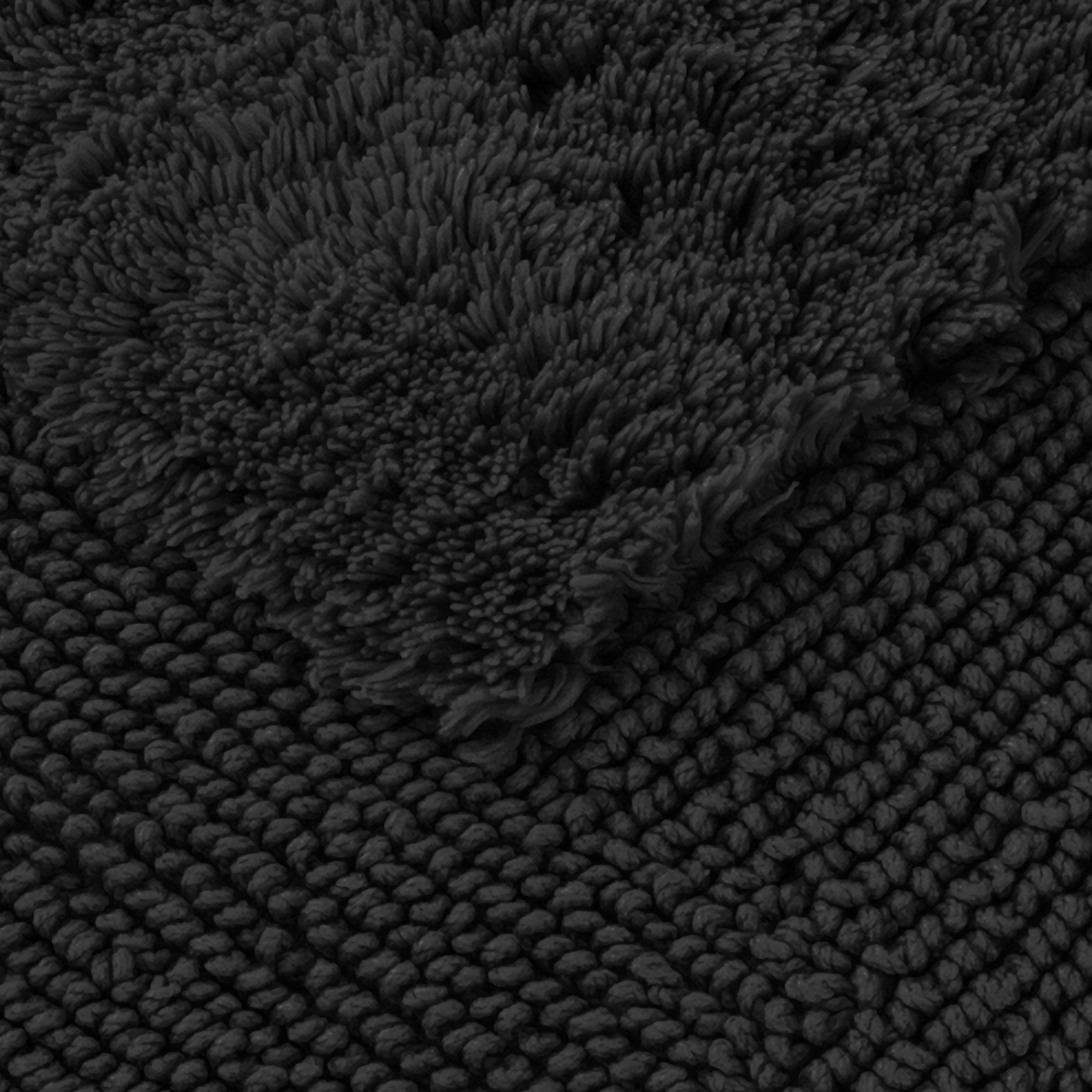 A fluffy, dark towel lies partially over a coarsely woven bathroom mat; a close-up highlights the dense pile and fiber textures of both textiles.