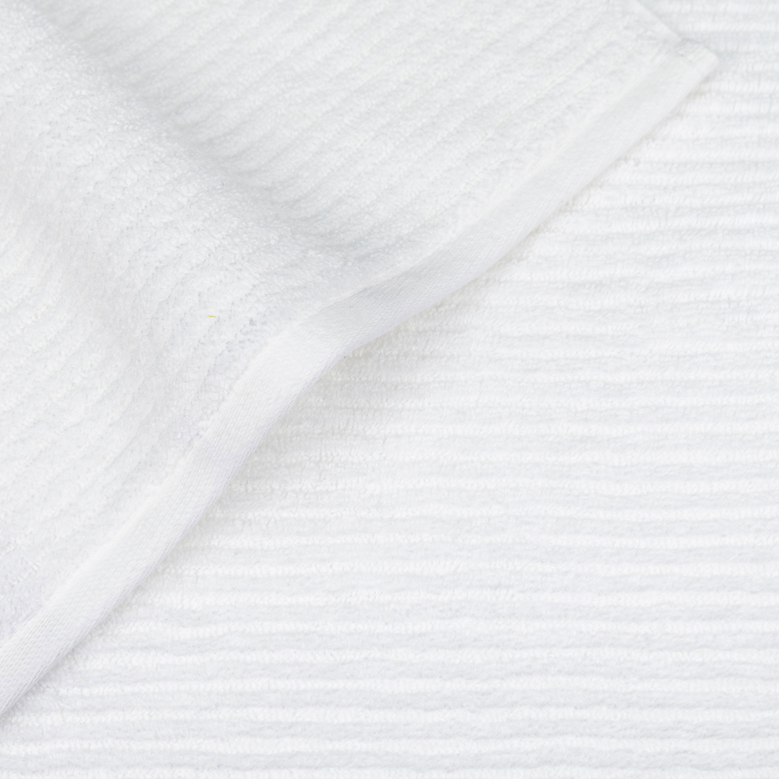 White towel with a folded corner revealing the hem; fine horizontal stripe pattern, laid flat on a light background.