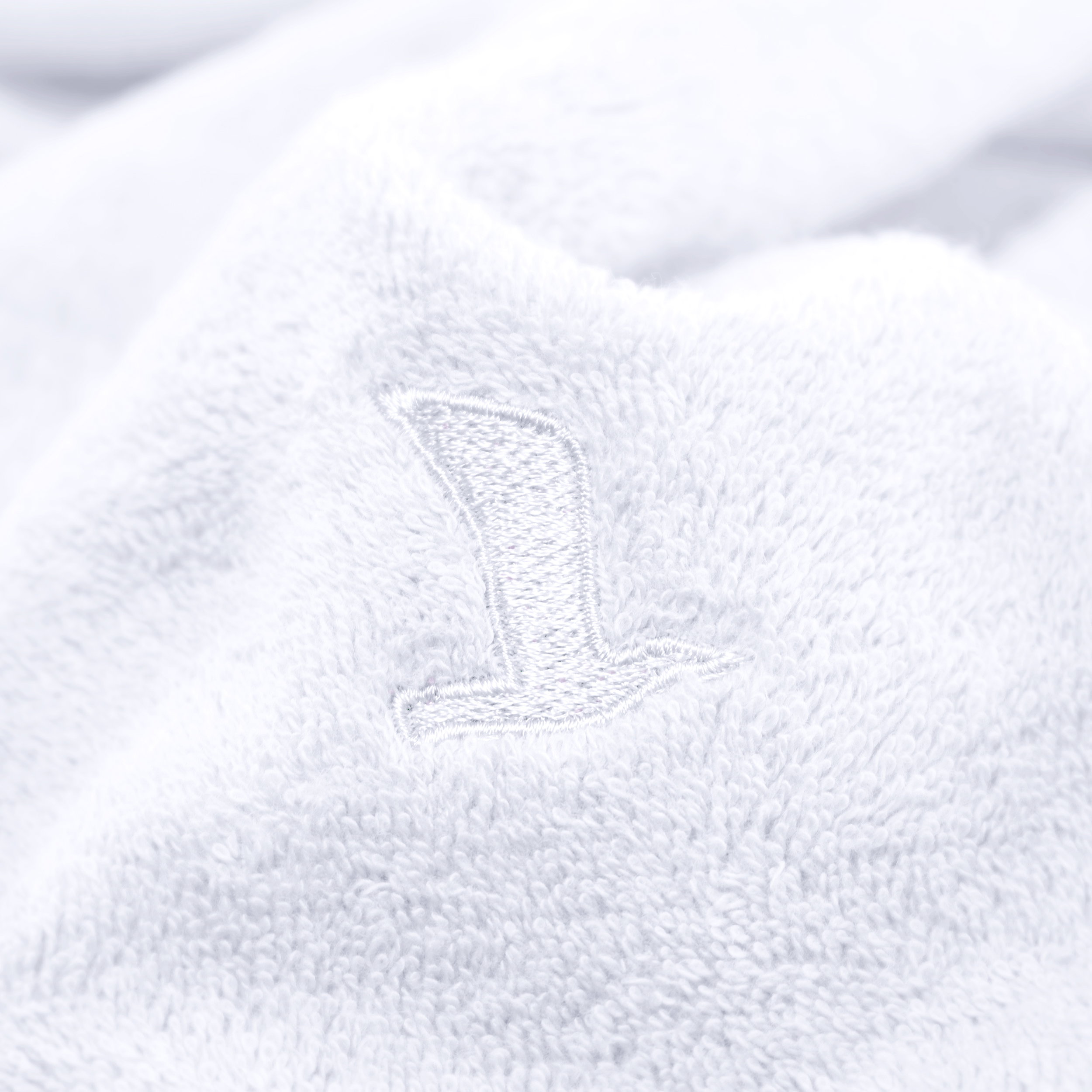 White terry towel with an embroidered “1” motif, draped casually; close-up highlights the soft texture and delicate embroidery, against a neutral light background.