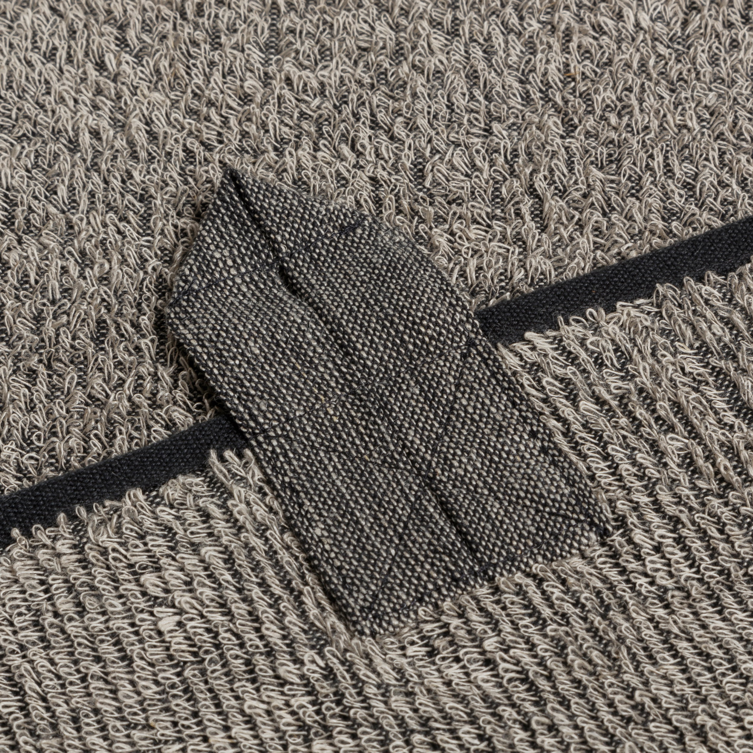 Frottierhandtuch mit angenähter Aufhängeschlaufe; liegt flach; Nahaufnahme der grauen, strukturierten Oberfläche mit dunklem Saum, typisches Badtextil.