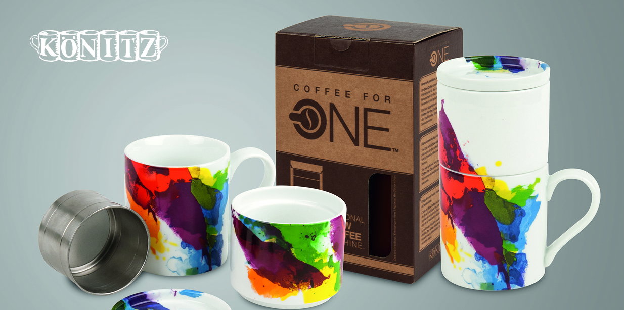 Porzellan-Kaffeebecher mit buntem Aquarelldruck; einer gestapelt, weitere geöffnet neben Metallfilter und Kartonverpackung. Produktaufnahme auf neutralem, hellgrauem Hintergrund.