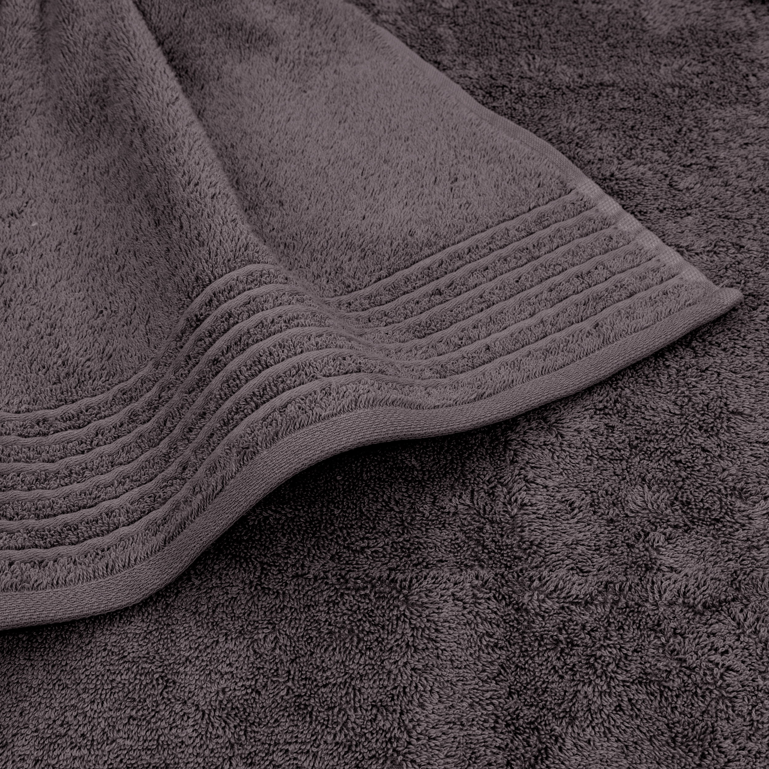 A folded terry towel lies on top of a second towel; the decorative border with parallel stripes is visible; soft, fluffy texture, bathroom setting.