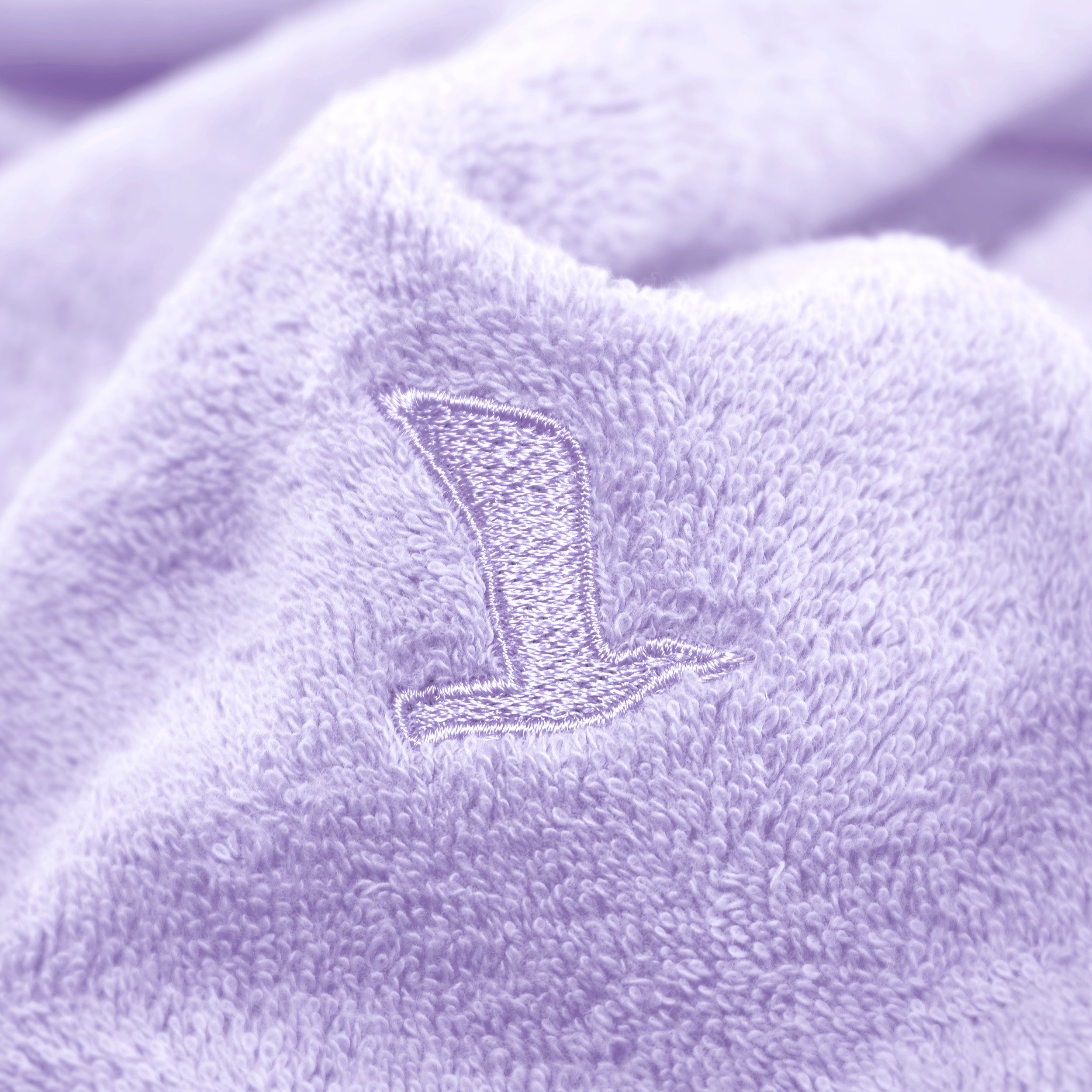Flauschiges hellviolettes Handtuch zeigt in Nahaufnahme ein gesticktes Möve-Vogelsymbol; weiche Frottee-Oberfläche, typisches Badezimmertextil.