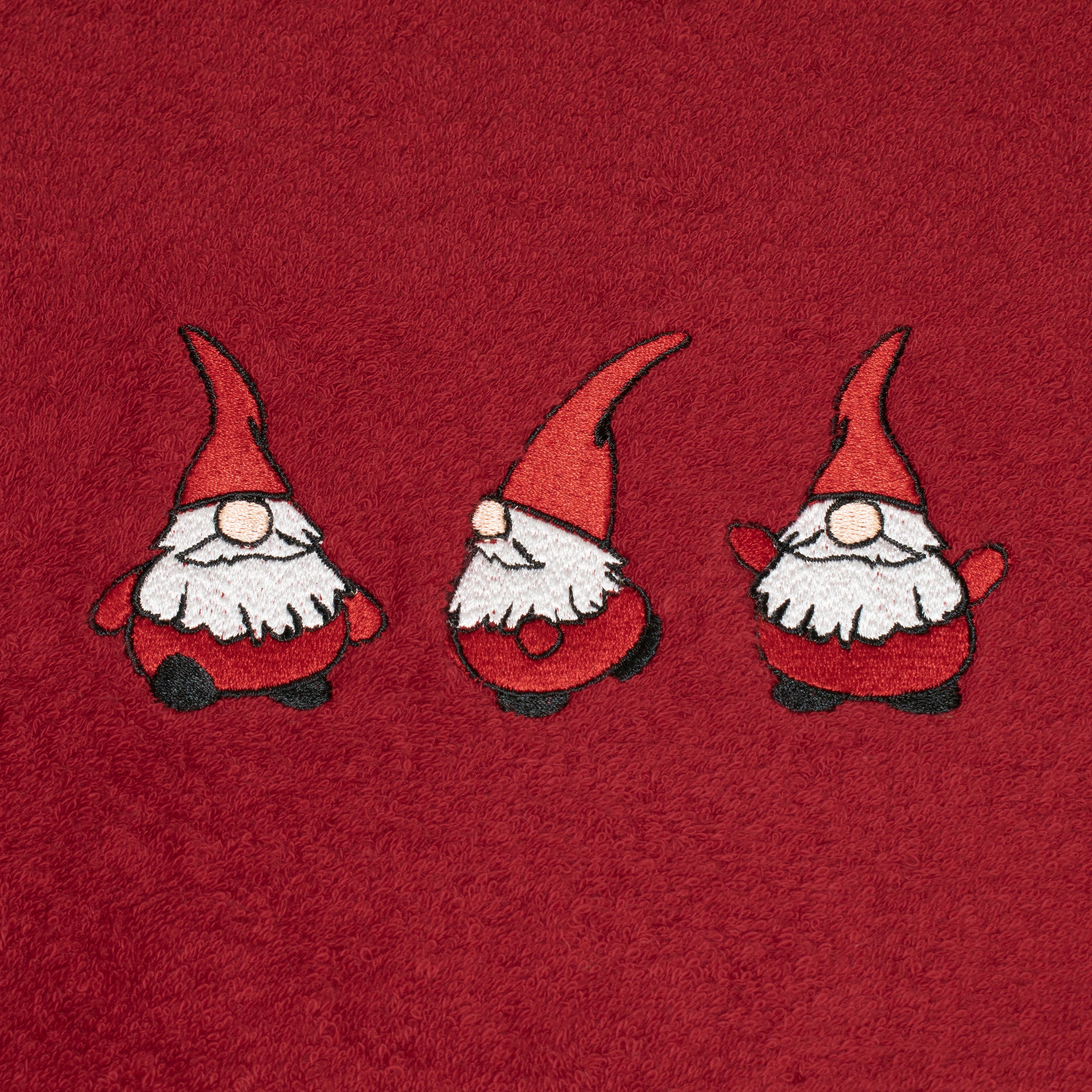 Red terry cloth towel with three elves embroidered side by side; the figures are in slightly different poses; solid-color background, bathroom accessory.