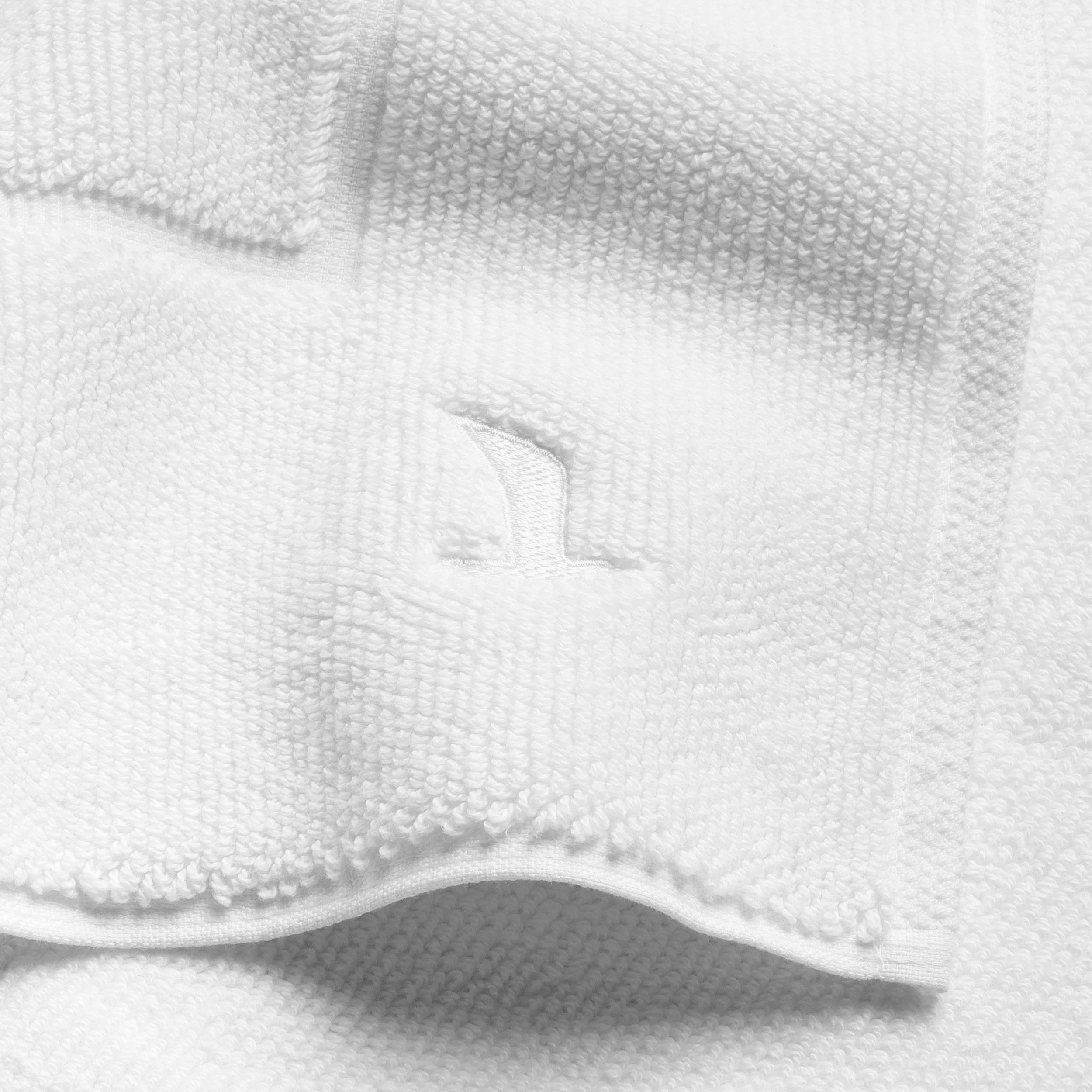 White, textured towel with embroidered seagull logo, slightly turned up and folded; close-up on a neutral background, presented as a bathroom textile.