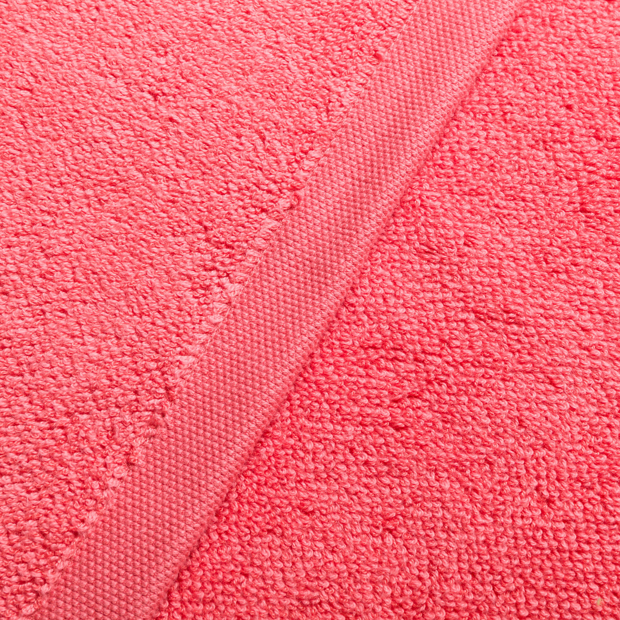 Handtuch – korallenfarbenes Frotteehandtuch liegt flach; diagonale, gewebte Saumkante sichtbar, betont weiche Schlaufenstruktur und textile Oberfläche.