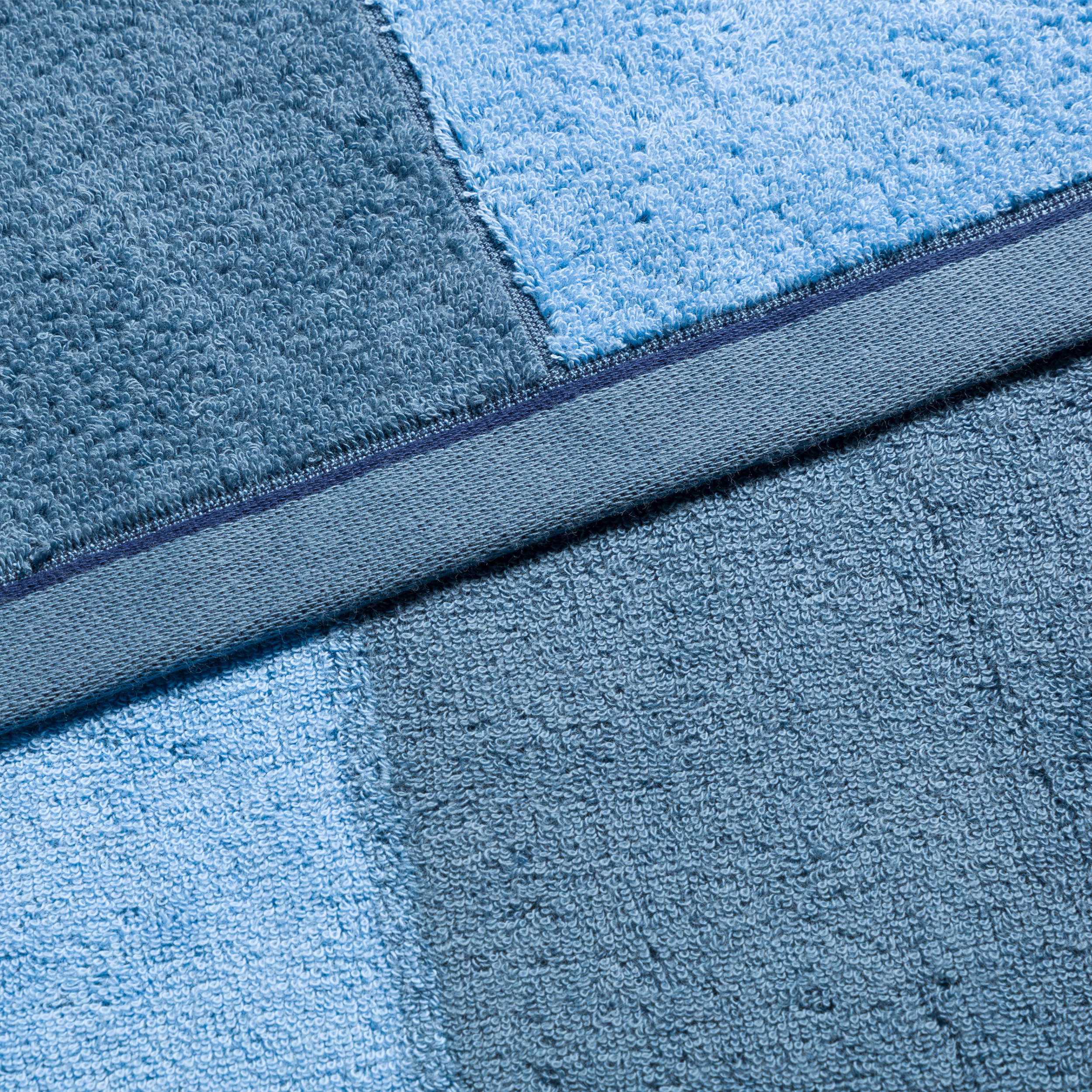 Towel in two shades of blue; lies flat, clearly showing texture and decorative stitching; close-up of a bathroom textile.