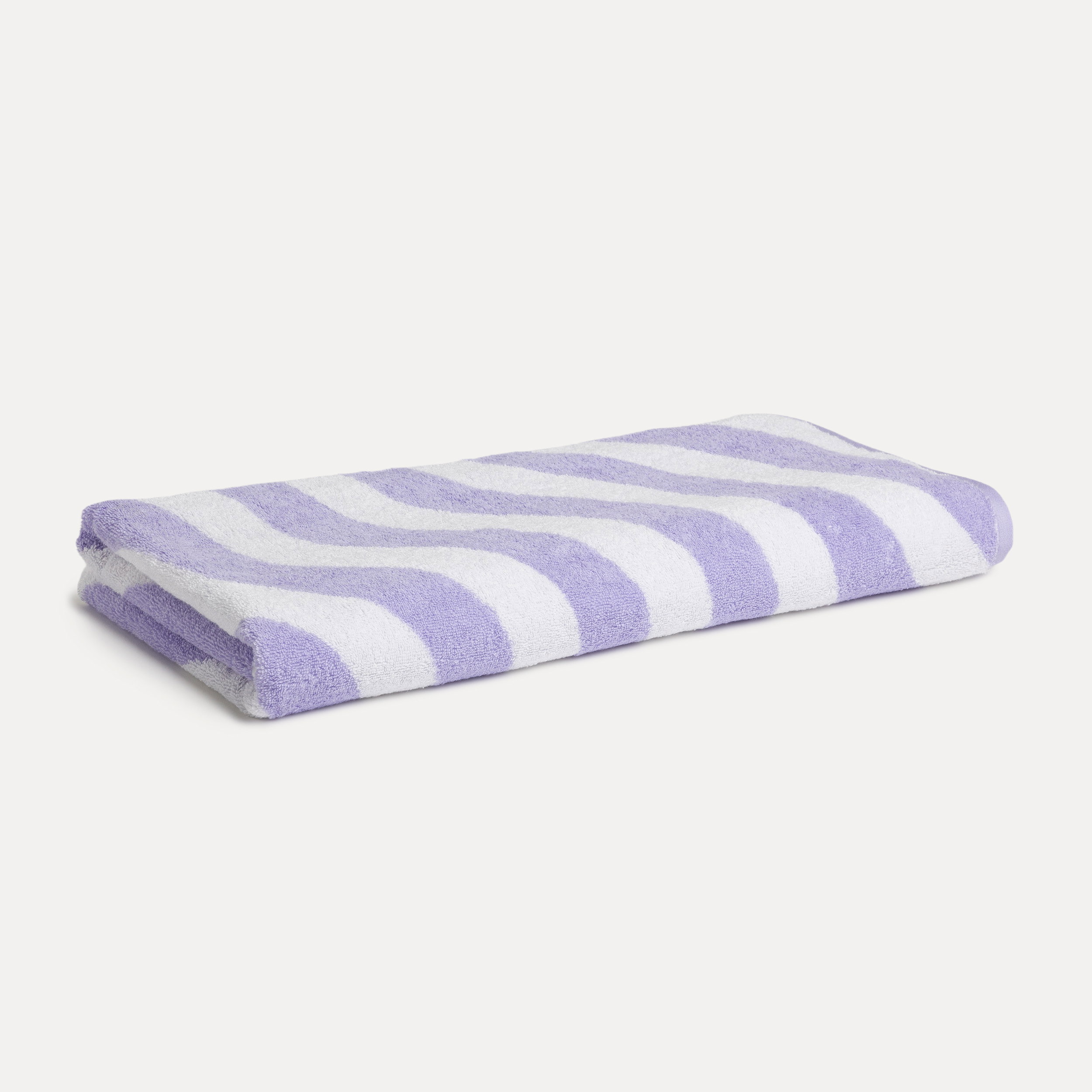 Folded terry towel lies flat; features a wavy purple-and-white striped pattern, soft, absorbent texture; presented on a neutral, light background as a bathroom accessory.